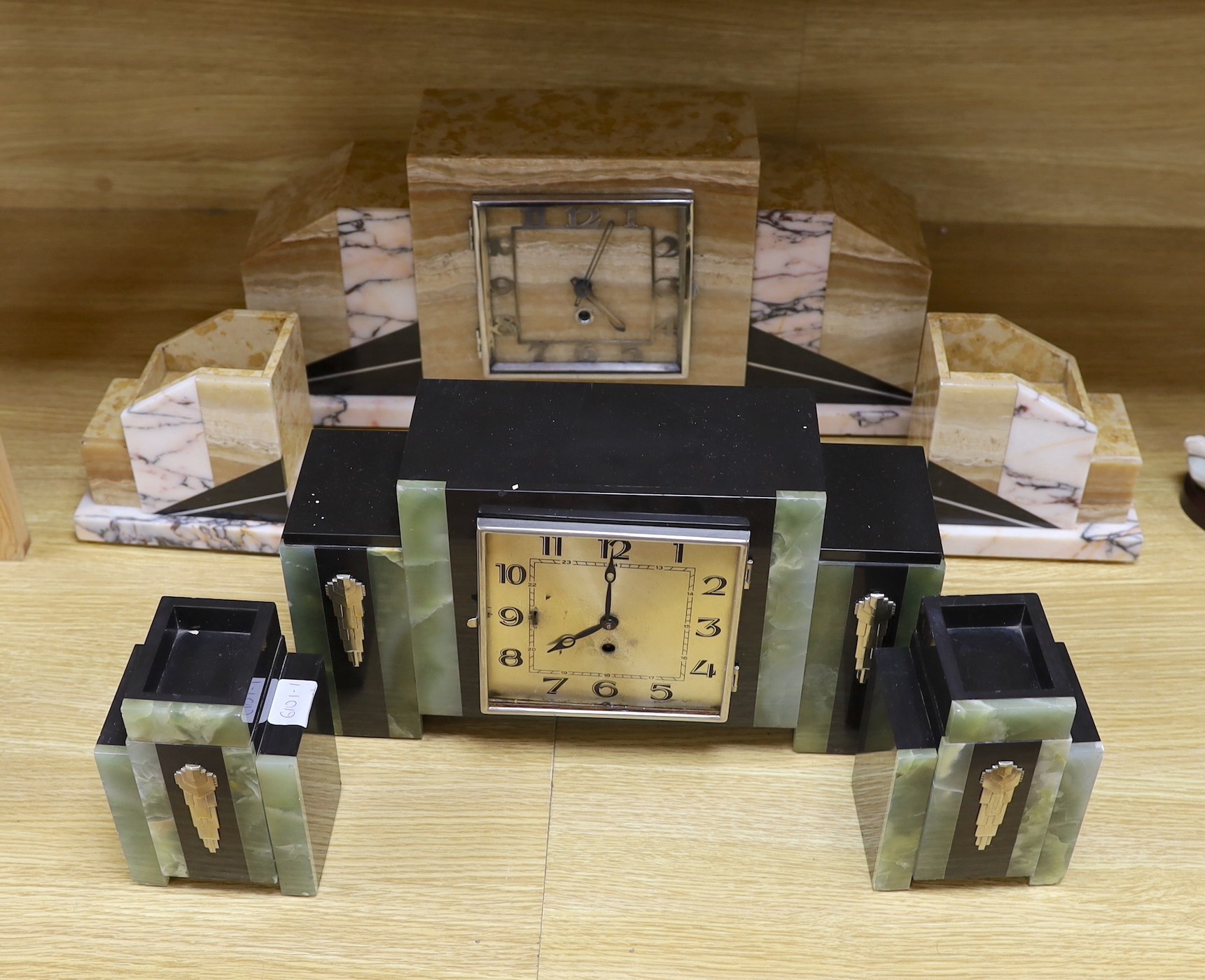 An Art Deco marble and onyx clock garniture, together with another stylised onyx Art Deco marble clock garniture with decorative silver-coloured reliefs